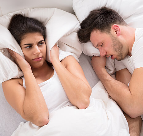 woman covering her ears with her pillow as her husband snores